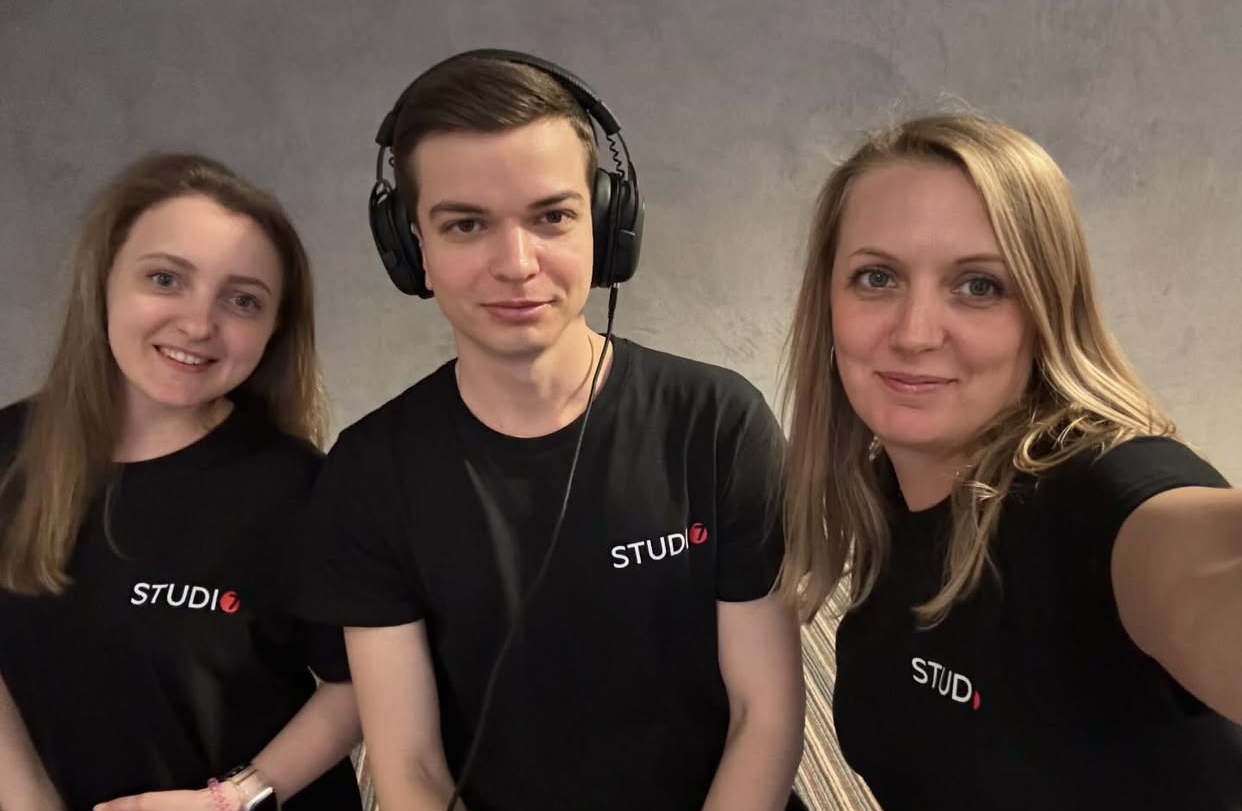 Three smiling production crew members wearing matching black "STUDIO 7" shirts pose together against a gray backdrop, representing the expert media team behind Scenester and Neyius Media projects.
